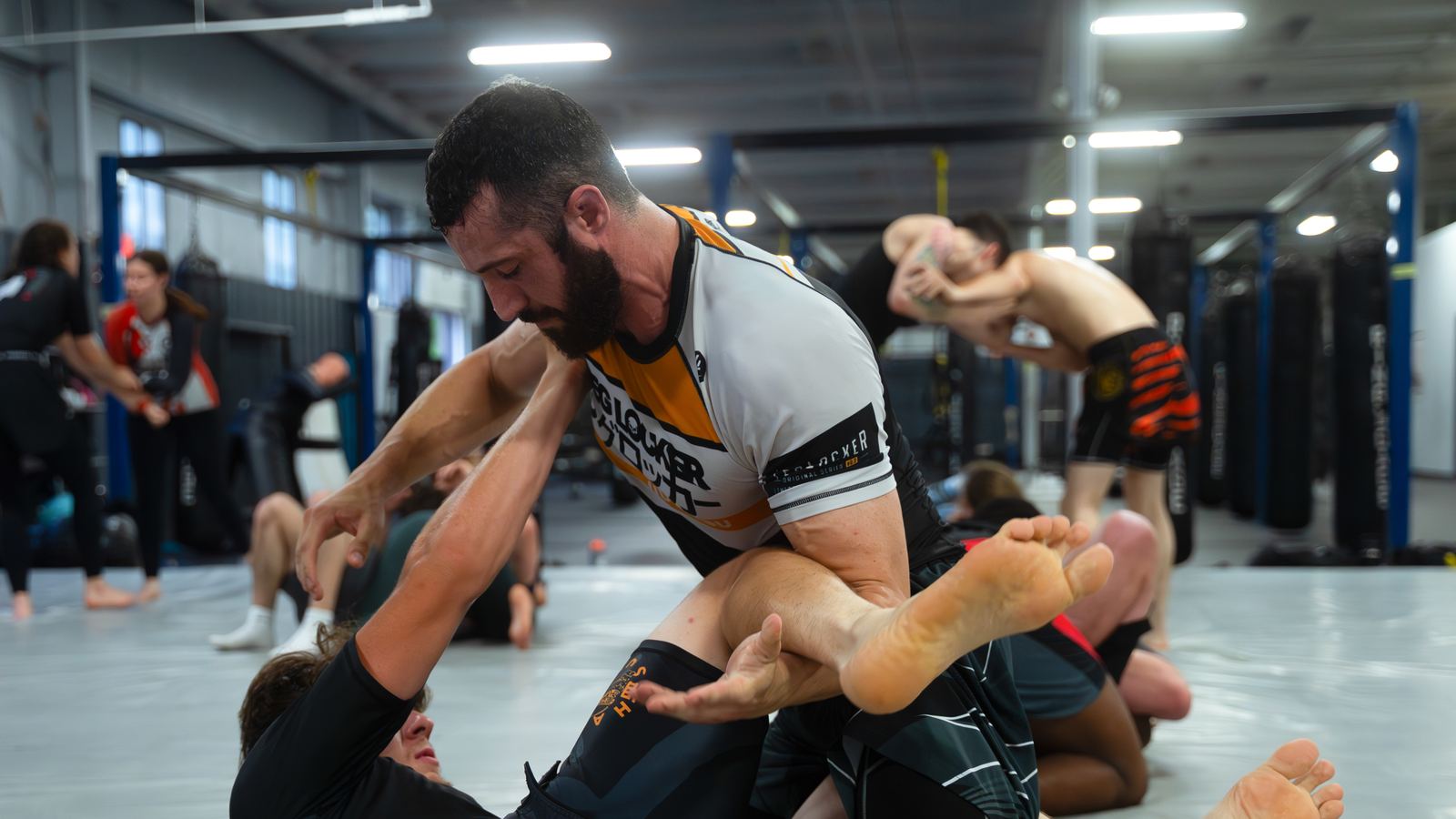 Two students in a live no-gi round, one working a leg entanglement on the mat.