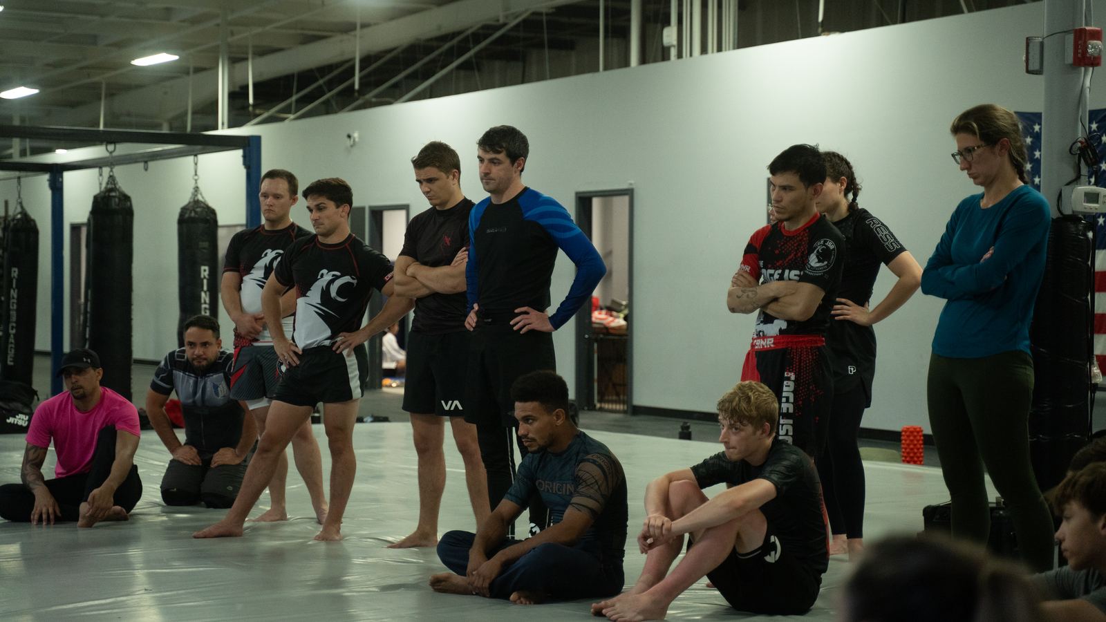 A TRITAC class standing and sitting on the mat watching a technique being taught.
