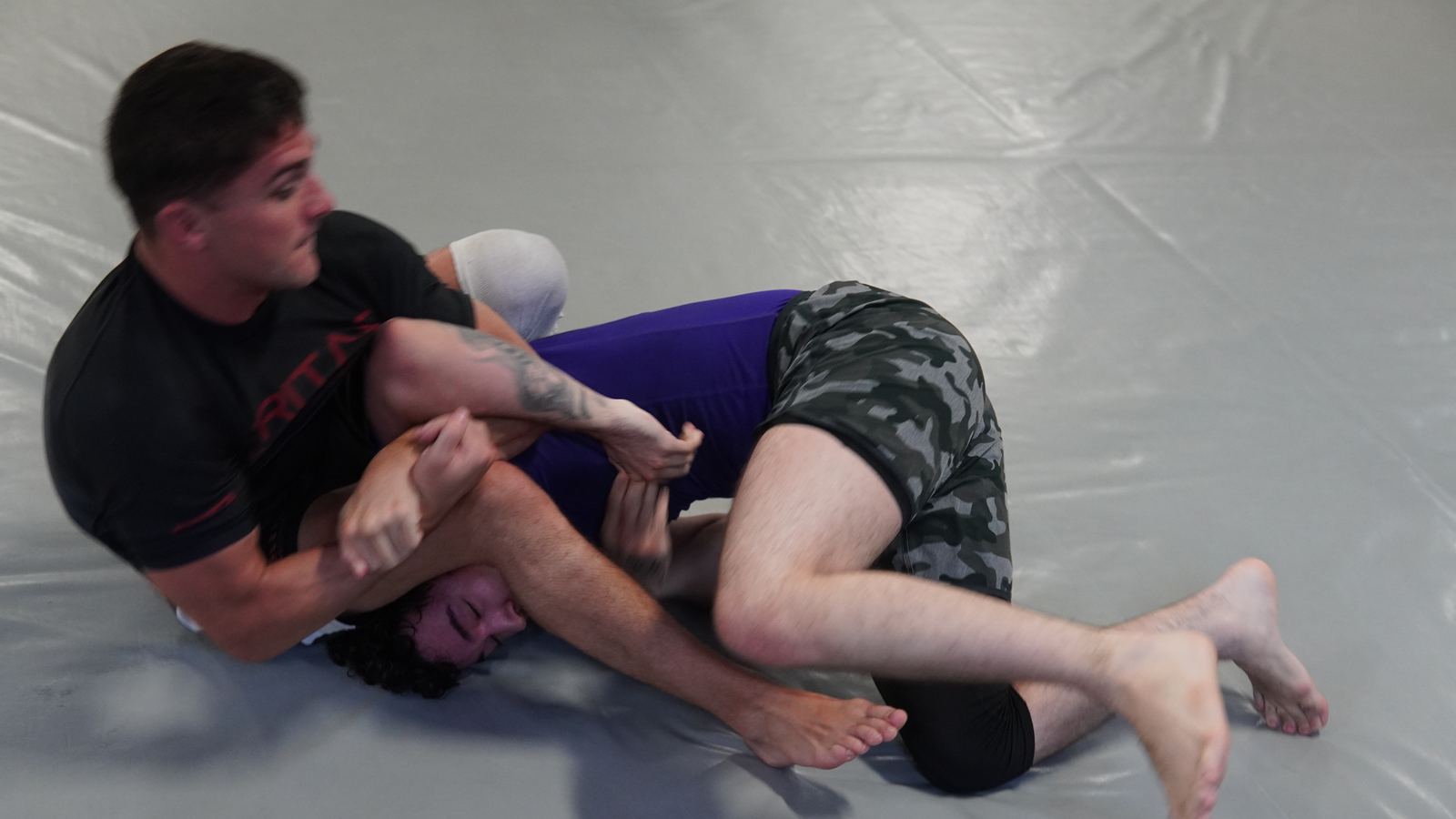 A grappler holding top control and attacking an arm during a live round.