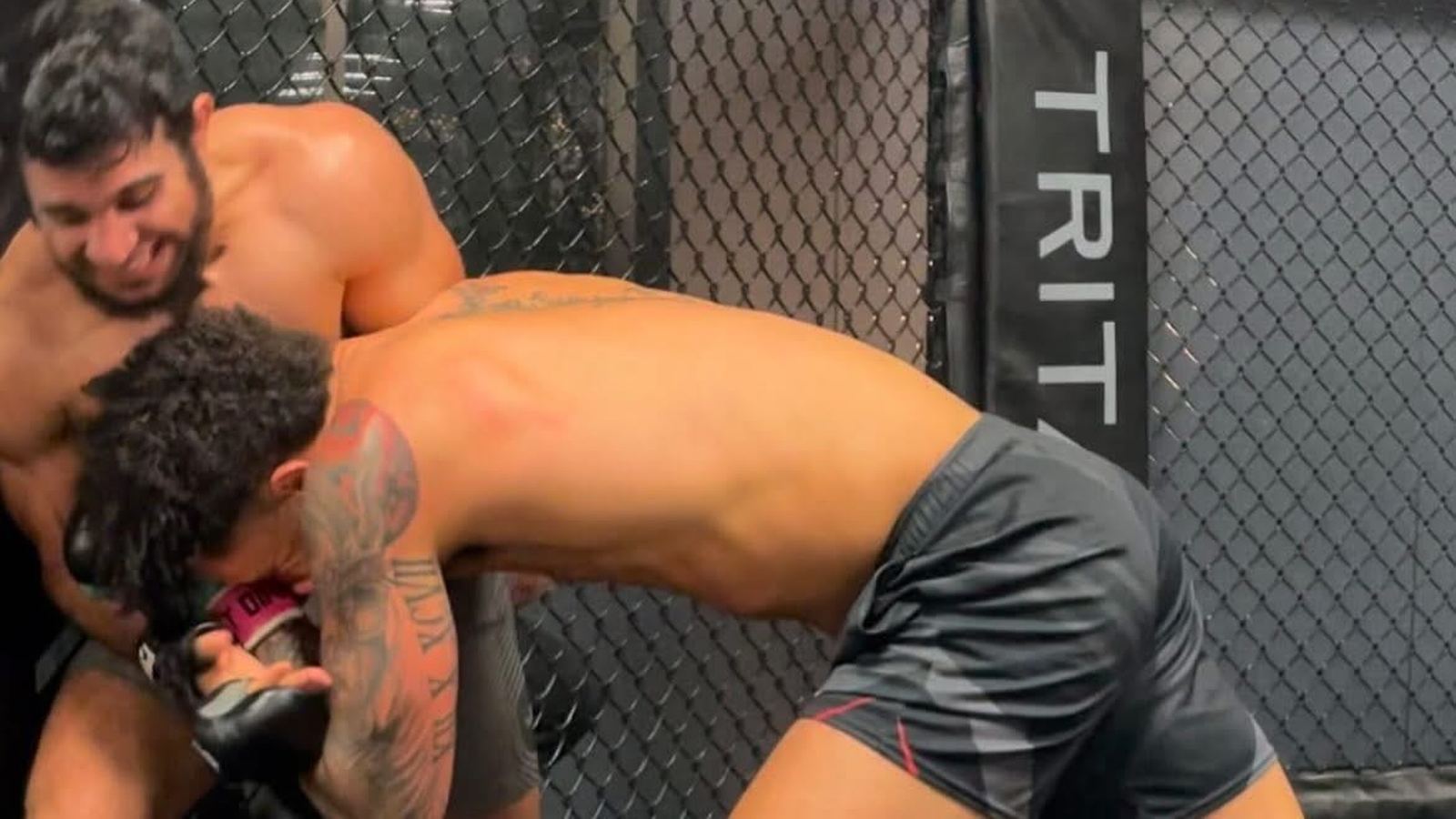 Two fighters working a body lock against the fence inside the TRITAC cage.