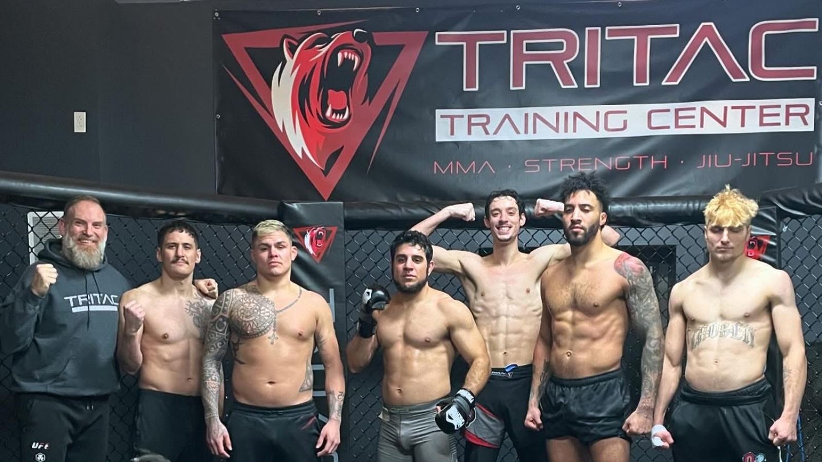 The TRITAC fight team lined up in the cage under the TRITAC Training Center banner.