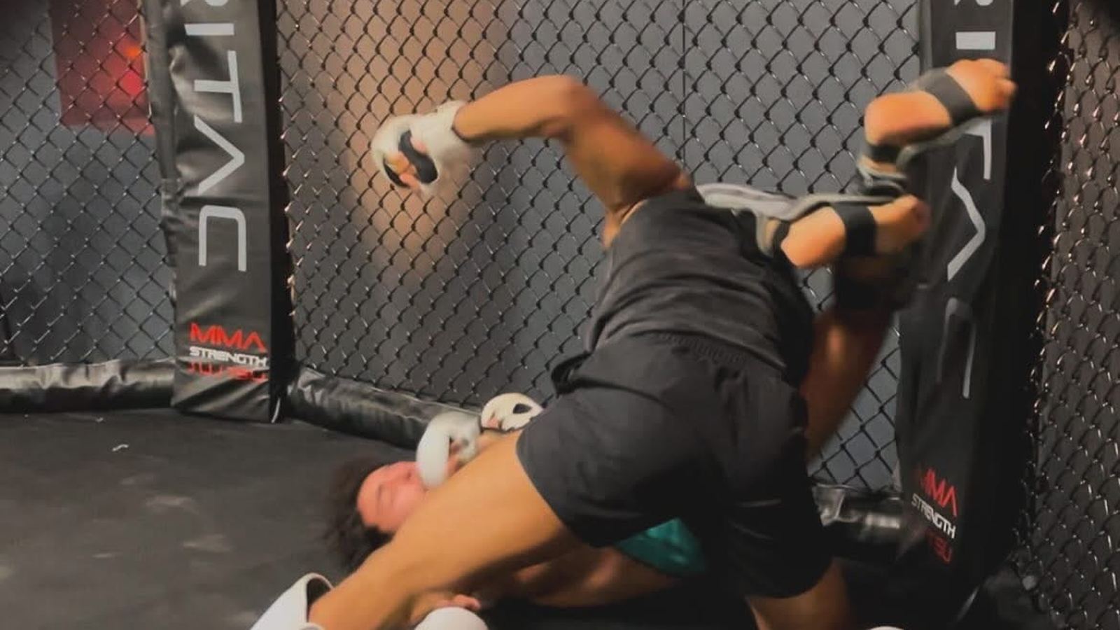 A fighter working from top position against the cage during a hard round.