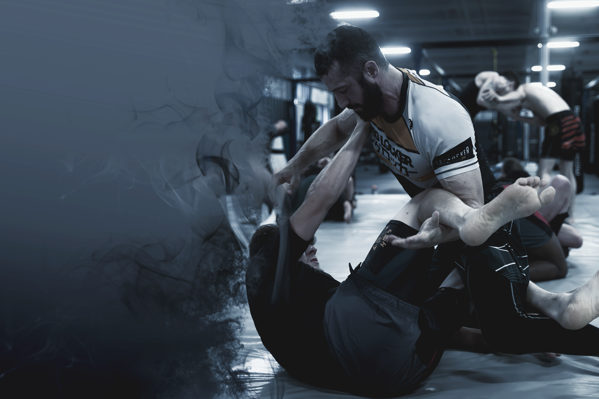 Members training ground grappling on the TRITAC mat, multiple groups in the background