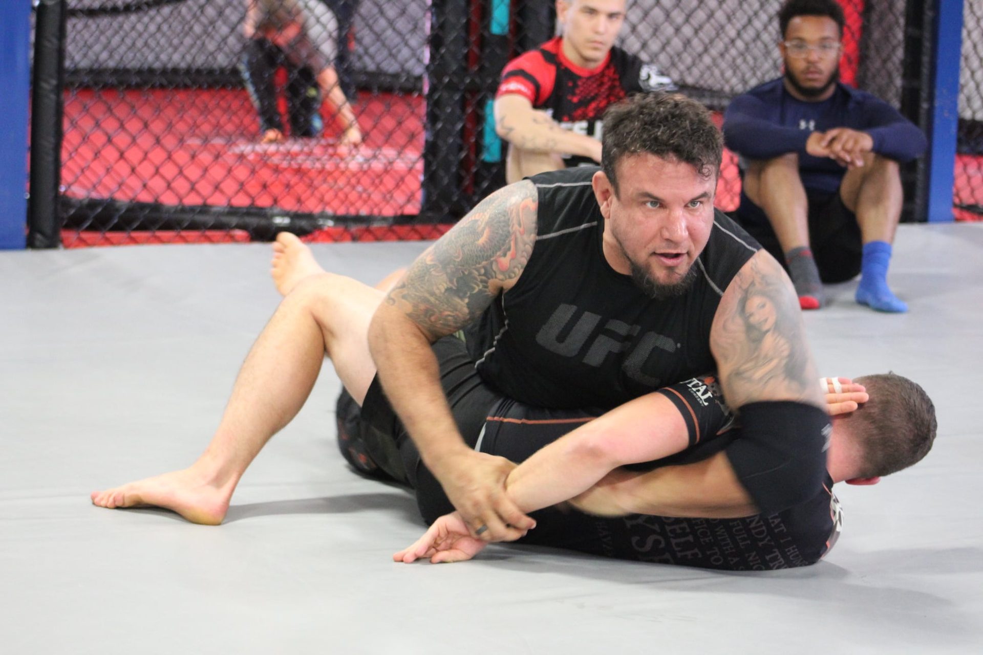 Frank Mir working side control in the TRITAC cage, students watching