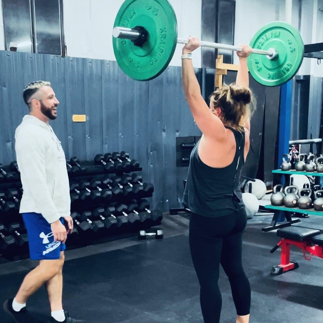 Coach watching a member do an overhead press on the TRITAC strength floor