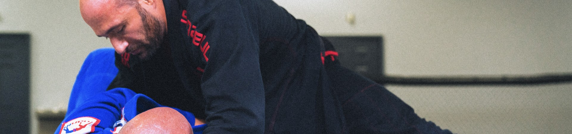 A student in a black gi holding heavy side control over a partner in a blue gi