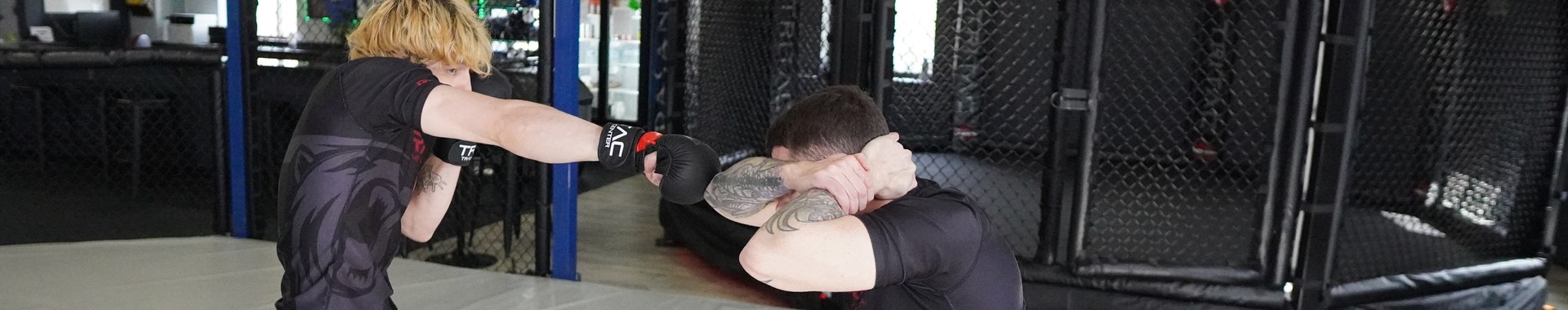 Two students trading strikes with gloves on, one landing a jab, cage and gym signage behind them