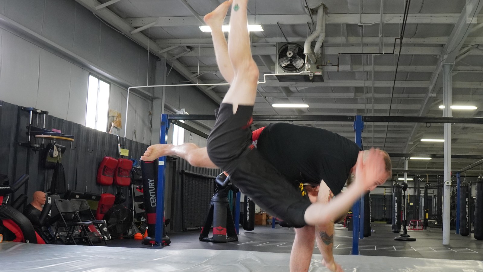 A coach finishing a throw, his partner upside down in the air above the mat.
