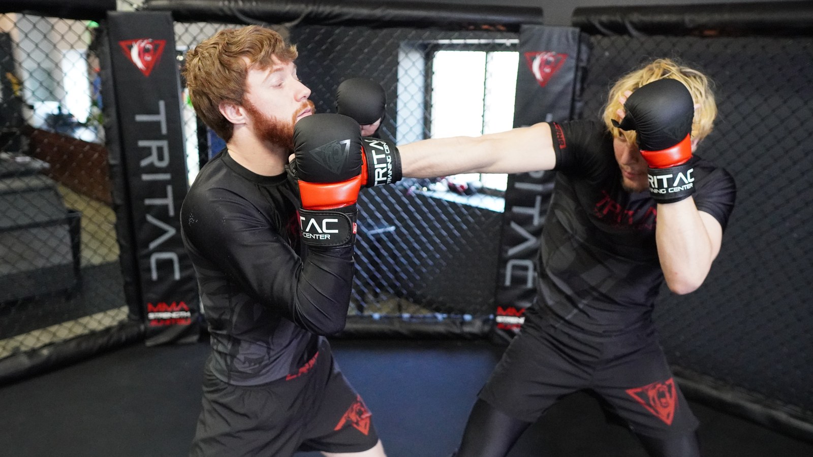 A student landing a straight punch during a live MMA round inside the TRITAC cage.